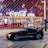 A sleek black sports car is parked in front of an illuminated arena entrance, with a large sign bearing the name of a famous beverage brand. The building features a modern, geometric facade with bright red and blue lights, creating a vibrant and lively atmosphere.