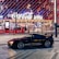 A sleek black sports car is parked in front of an illuminated arena entrance, with a large sign bearing the name of a famous beverage brand. The building features a modern, geometric facade with bright red and blue lights, creating a vibrant and lively atmosphere.